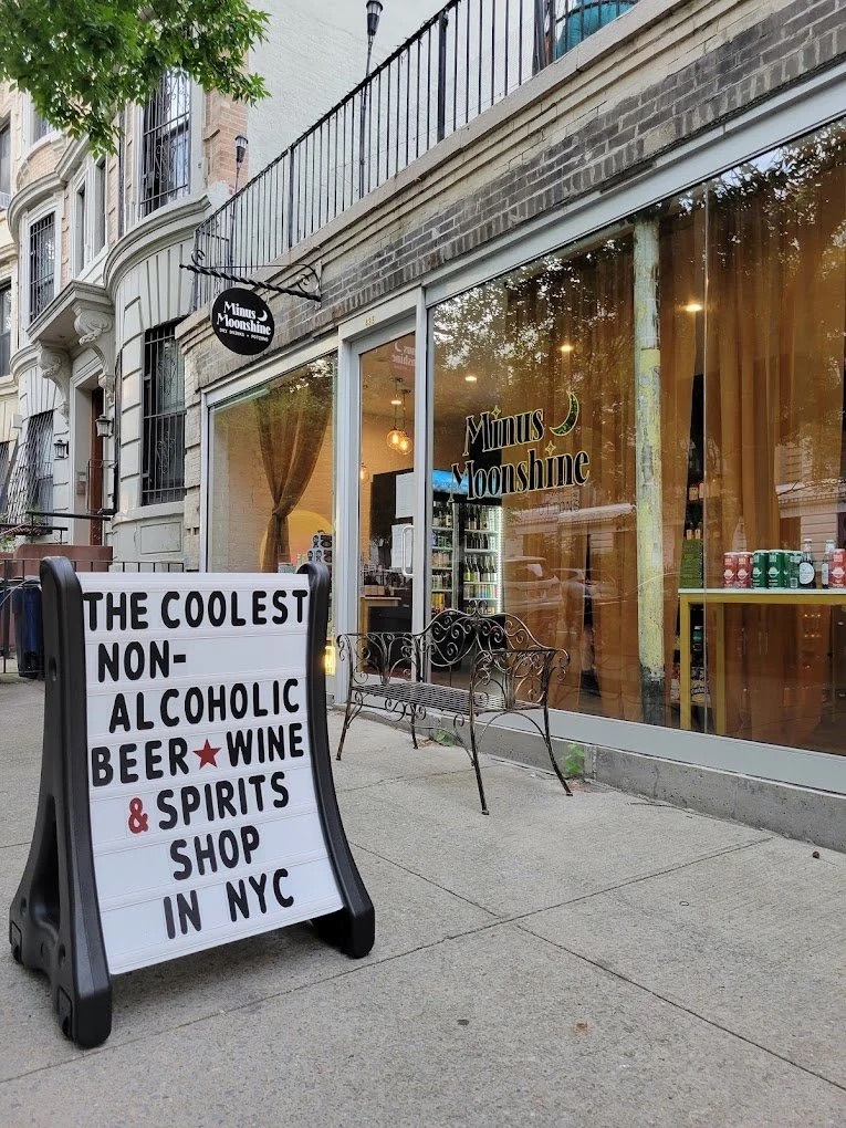 Minus Moonshine storefront in Brooklyn with a sidewalk sign reading "The coolest non-alcoholic beer, wine & spirits shop in NYC"